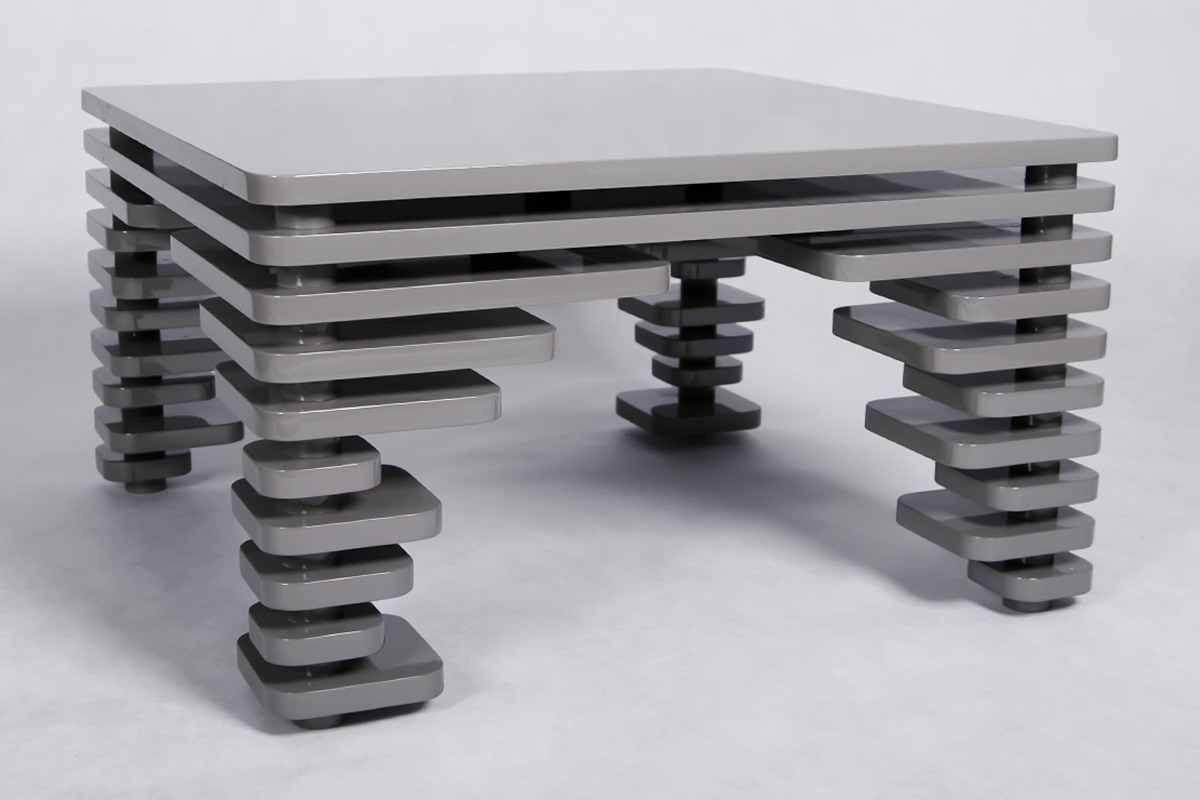 Nowoczesny stolik kawowy w odcieniach szarości o geometrycznej konstrukcji z poziomych płyt i kwadratowych nóg, na jednolitym tle.