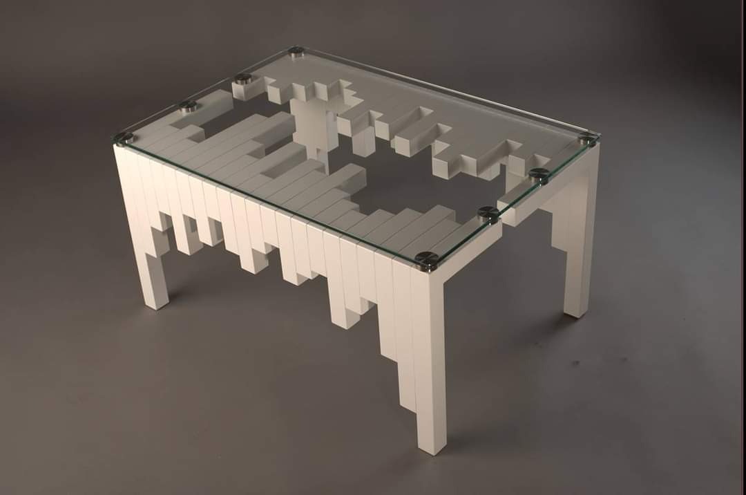 Biały stolik kawowy z geometryczną podstawą i szklanym blatem, widoczne metalowe mocowania blatu, nowoczesny design na szarym tle.