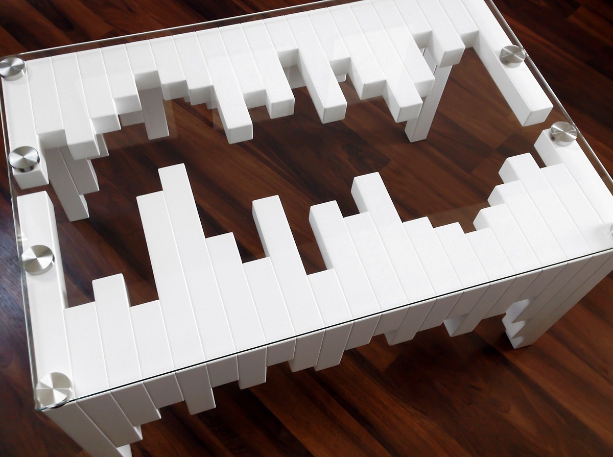 Stolik kawowy z białymi, prostokątnymi elementami tworzącymi geometryczny wzór wokół przezroczystego blatu, na tle drewnianej podłogi.