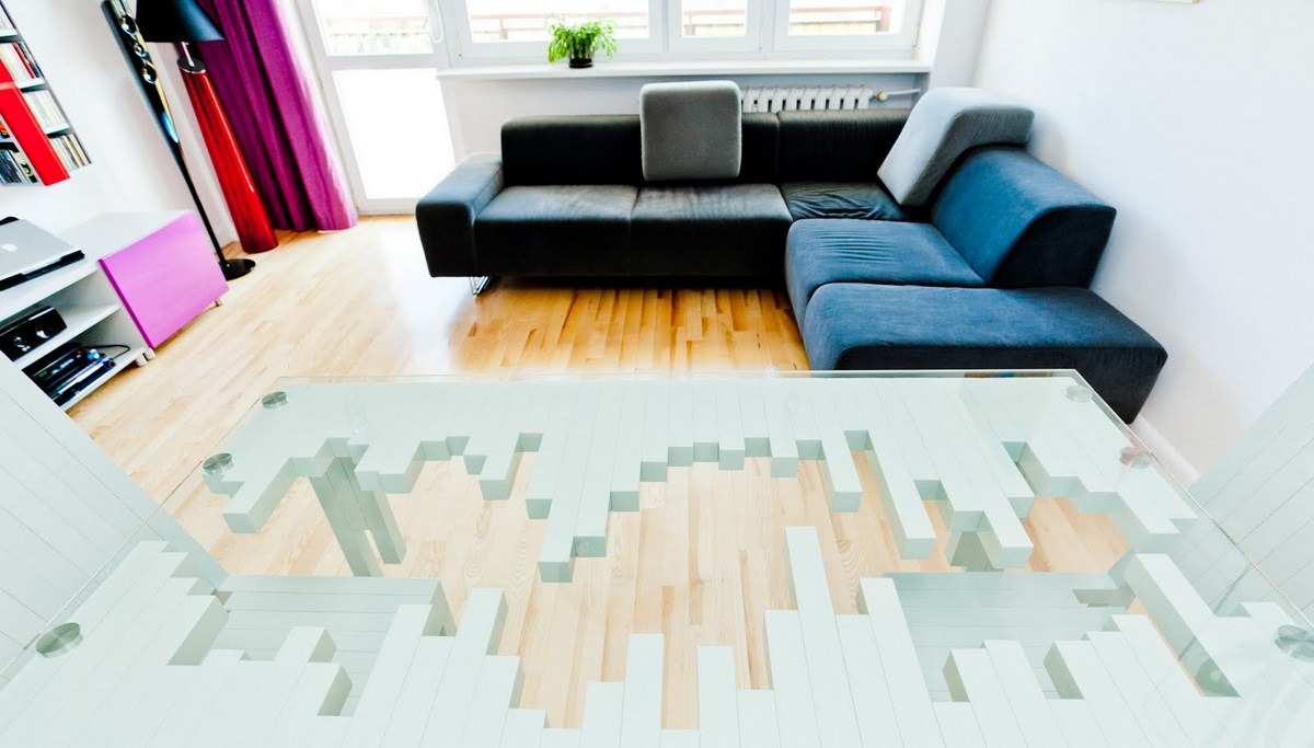 Nowoczesny salon z drewnianą podłogą, narożną sofą w odcieniach szarości i czerni oraz unikalnym, szklanym stołem z geometryczną podstawą.