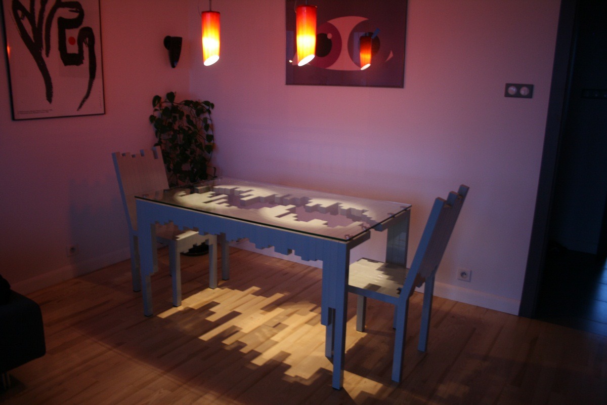 Stół i krzesła z motywem cityscape, wykonane na zamówienie, oświetlone ciepłym światłem lamp wiszących, rzucające geometryczne cienie na parkiet.