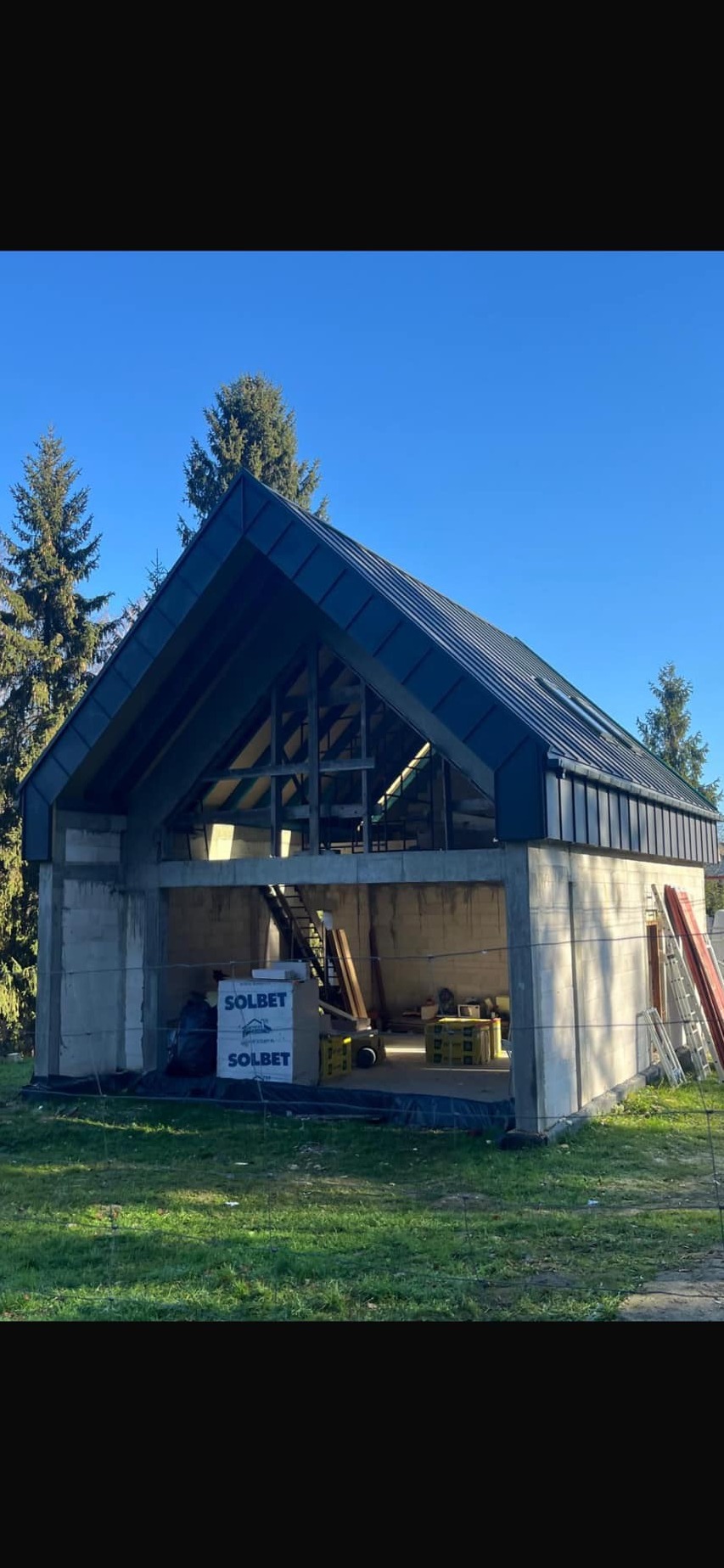 Budynek w trakcie budowy z zamontowaną konstrukcją dachu pokrytą blachą na tle błękitnego nieba, widoczne materiały budowlane Solbet