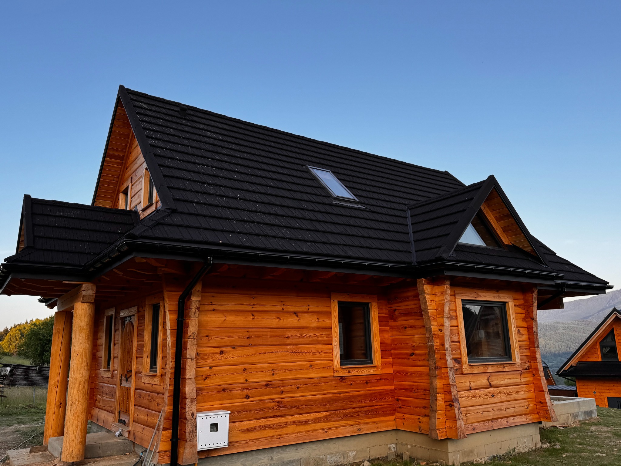 Nowoczesny dom z bali z ciemnym dachem i oknem dachowym, widok z dołu na tle błękitnego nieba.