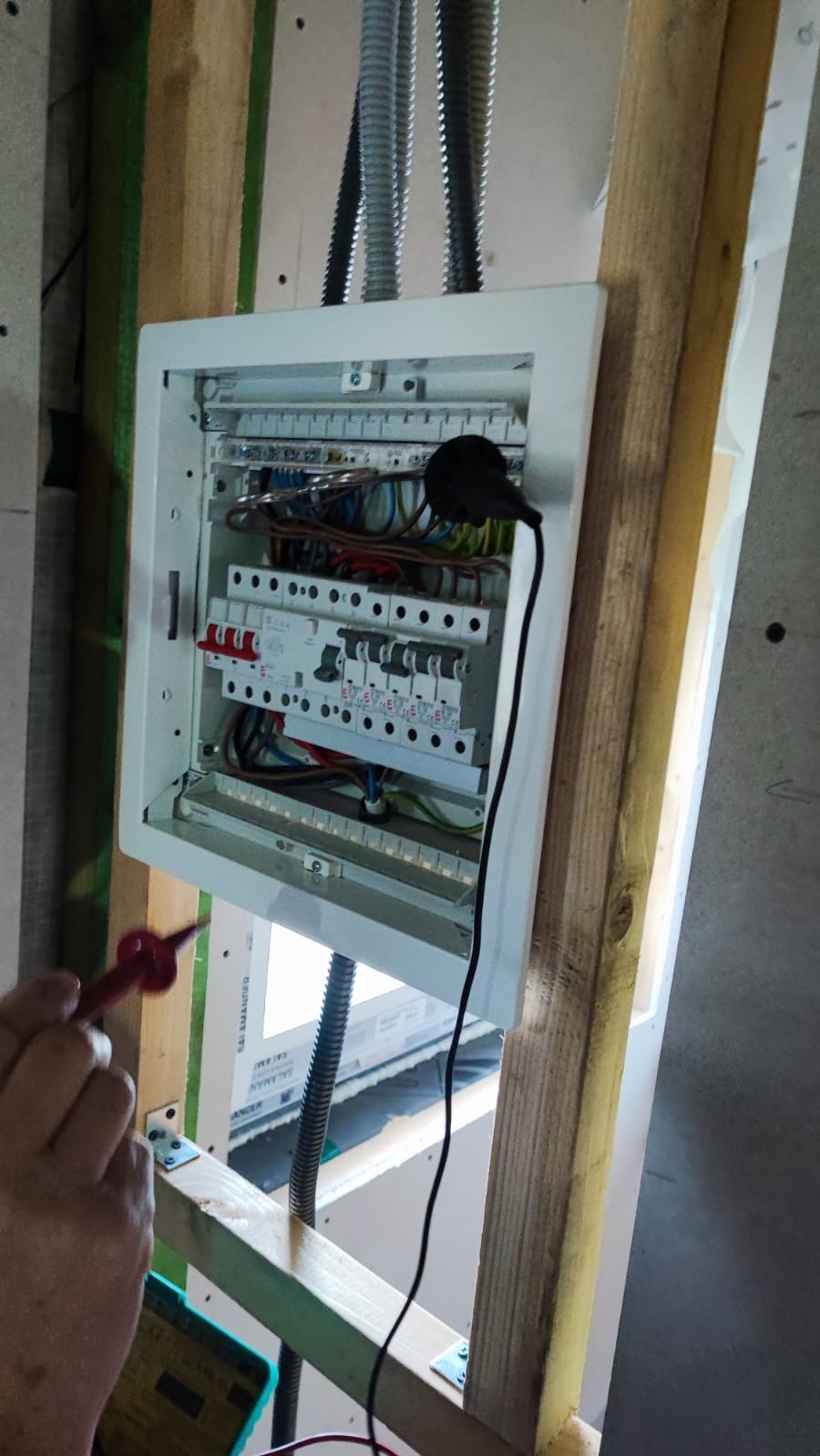 Otwarta skrzynka rozdzielcza z zainstalowanymi bezpiecznikami i przewodami, sprawdzana próbnikiem napięcia w surowym wnętrzu budynku.