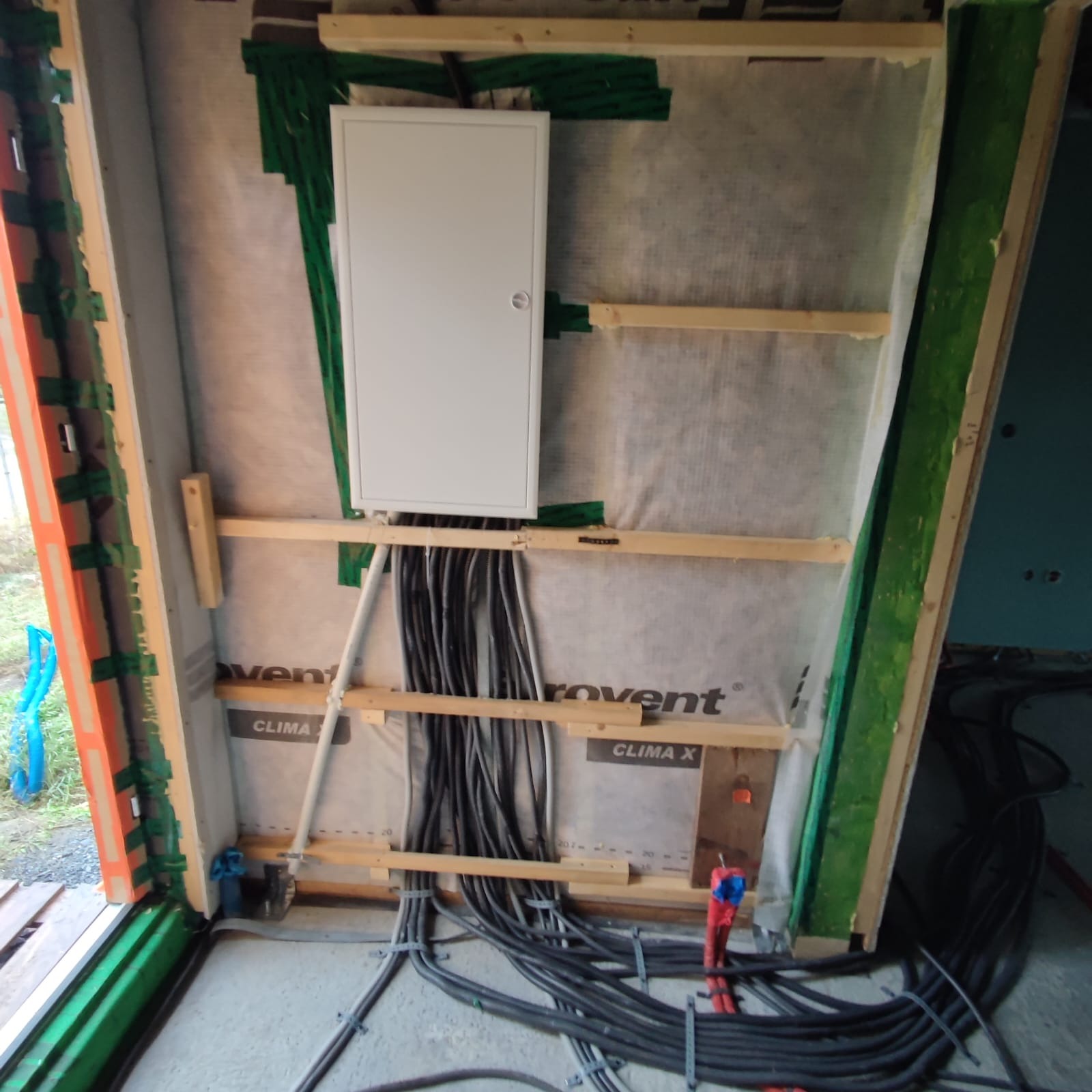 Rozdzielnica elektryczna z podłączonymi kablami w surowym wnętrzu, widoczne elementy konstrukcyjne ściany i izolacji.