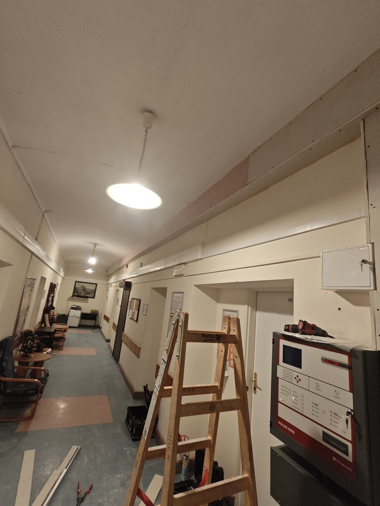 Korytarz w trakcie montażu instalacji elektrycznej: widoczna drabina, przewody, skrzynka alarmowa Polon 4900 i narzędzia elektryczne.