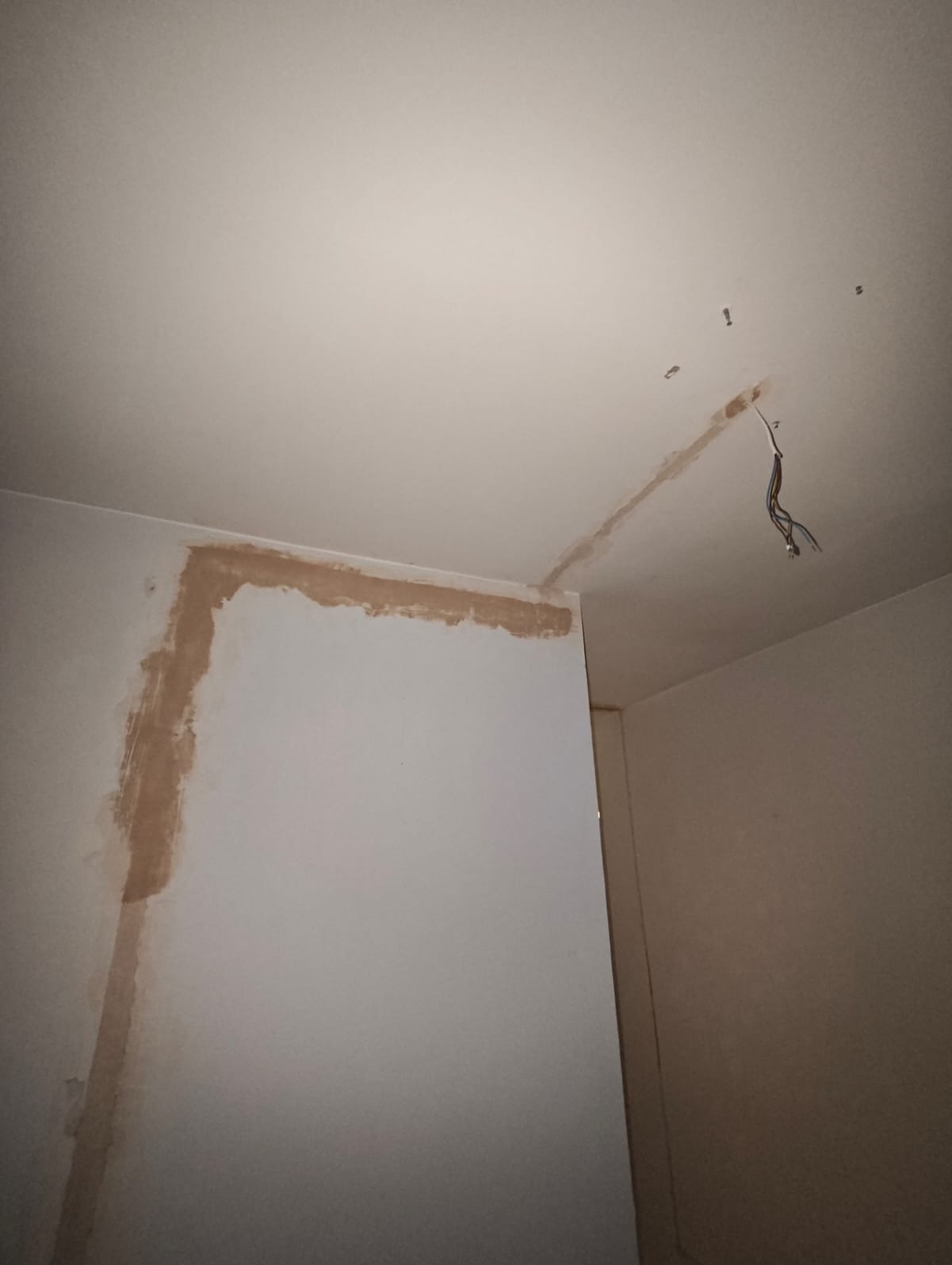 Fragment wnętrza w trakcie remontu: przewody elektryczne wystające z sufitu, ślady szpachli na ścianach i suficie.