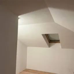 Poddasze po gładziowaniu i malowaniu na jasny odcień, widoczne drewniane okno dachowe i fragment drewnianej podłogi.