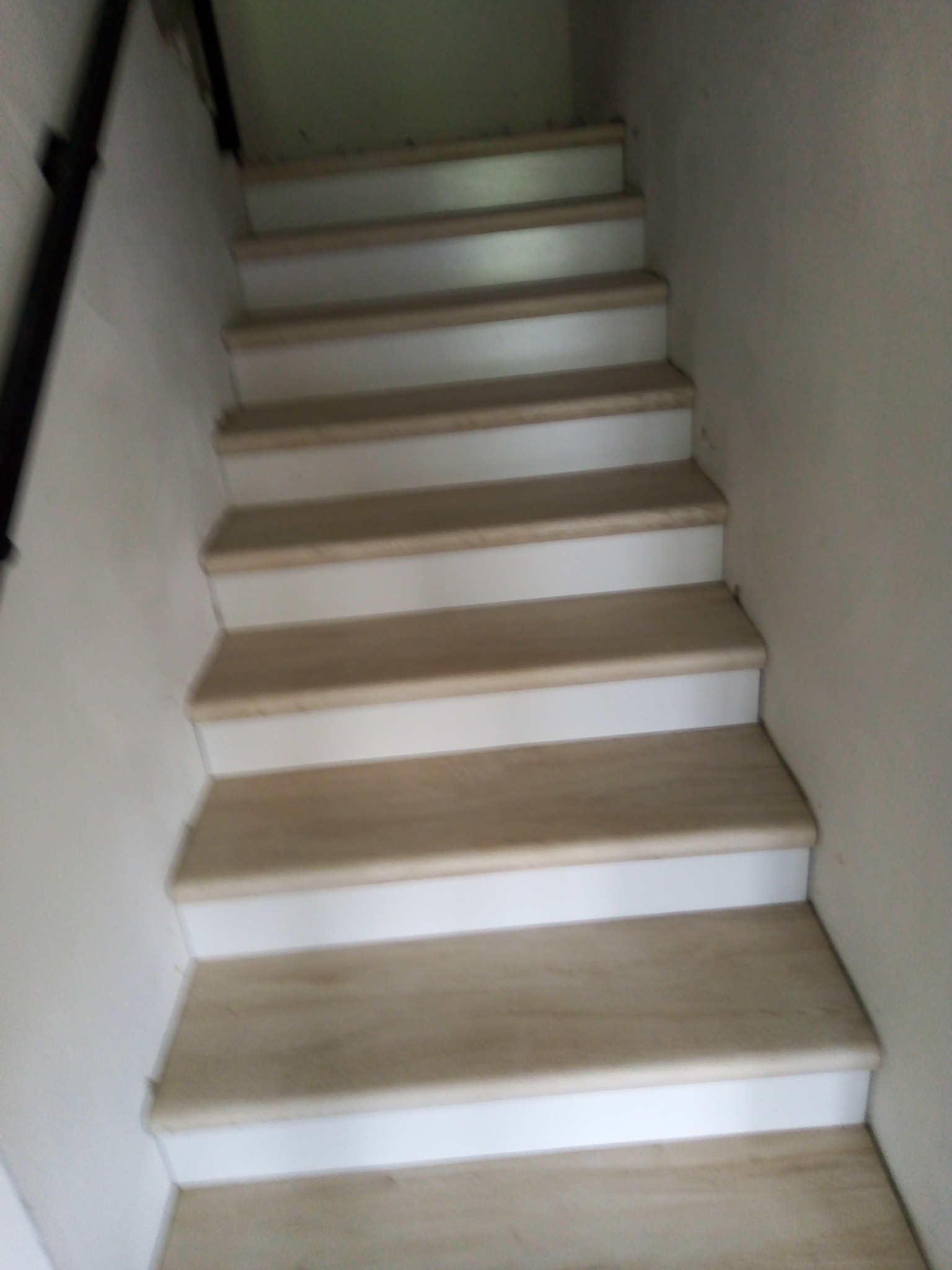 Schody wewnętrzne z drewnianymi stopniami i białymi podstopnicami, widok z dołu.