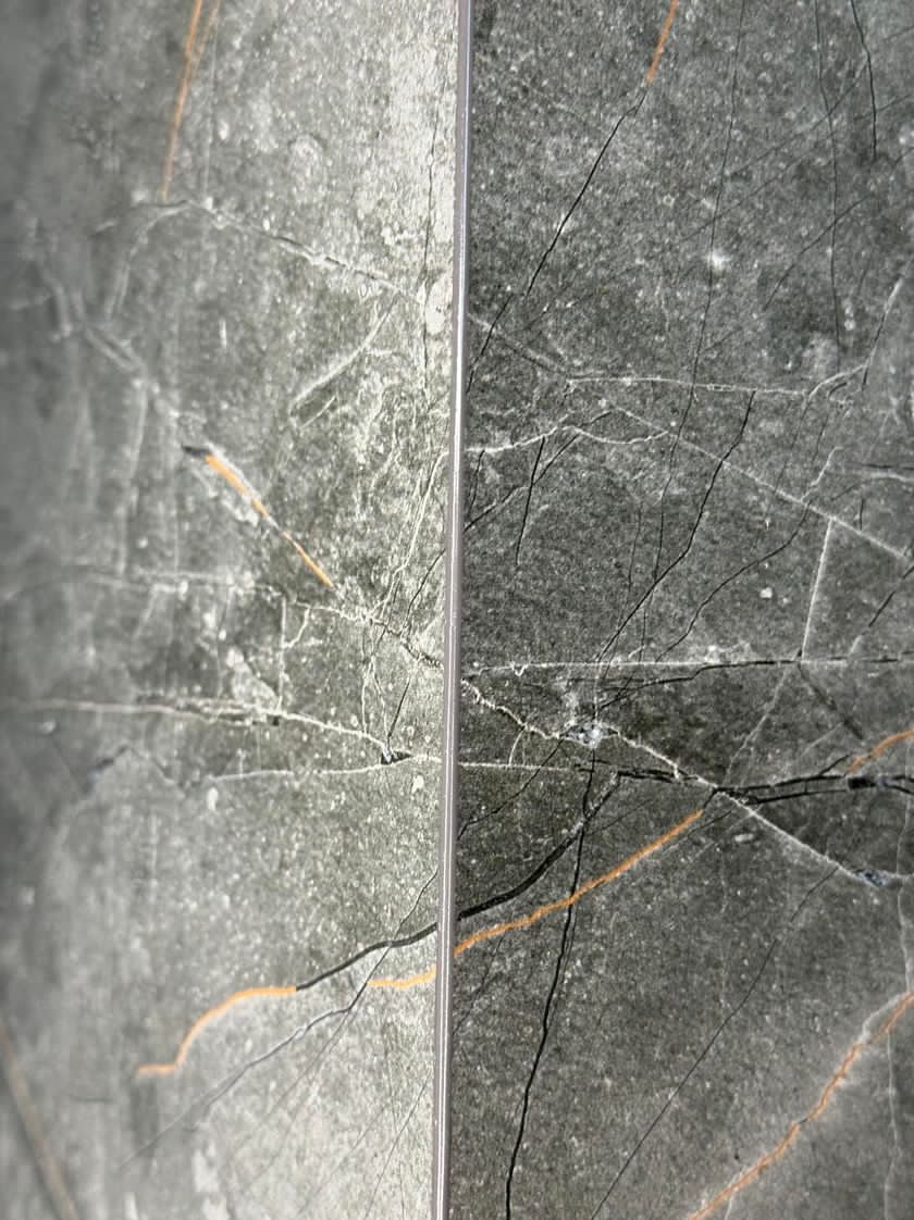 Dwie płytki z szarego marmuru z żyłkami w odcieniach czerni i pomarańczy, ułożone obok siebie z widoczną spoiną.