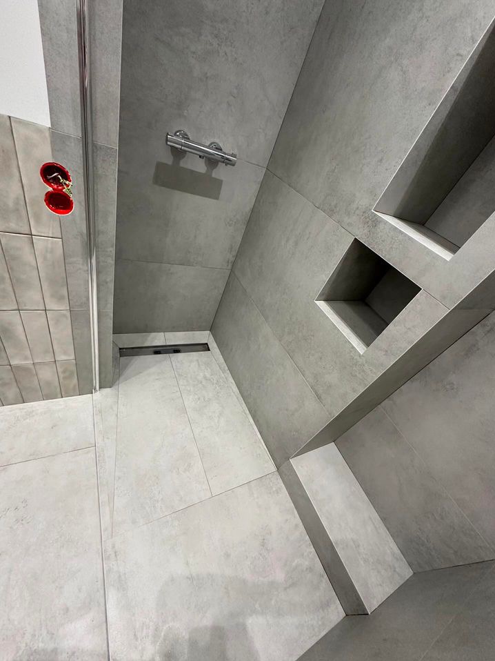 Wykończona łazienka w odcieniach szarości w Warszawie, z kabiną prysznicową walk-in, odpływem liniowym i wnękami w ścianie wyłożonymi płytkami.