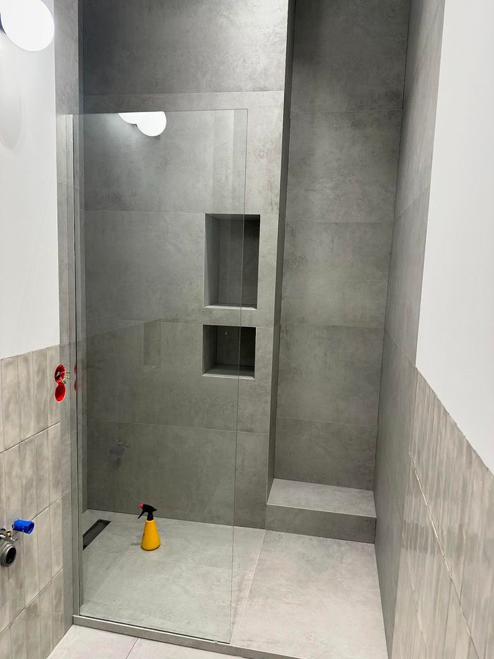 Nowoczesna kabina prysznicowa z szarymi płytkami, wnękami w ścianie i żółtym spryskiwaczem na podłodze