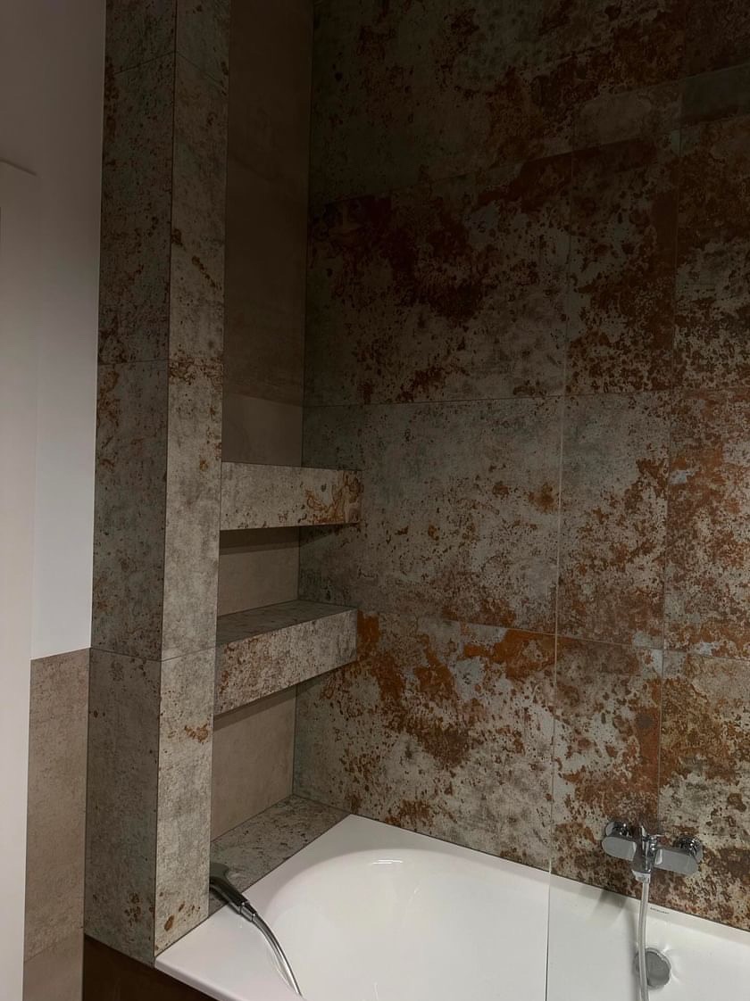 Wykończona łazienka z wanną i wnęką z półkami wyłożoną płytkami imitującymi rdzę, widoczna bateria wannowa.