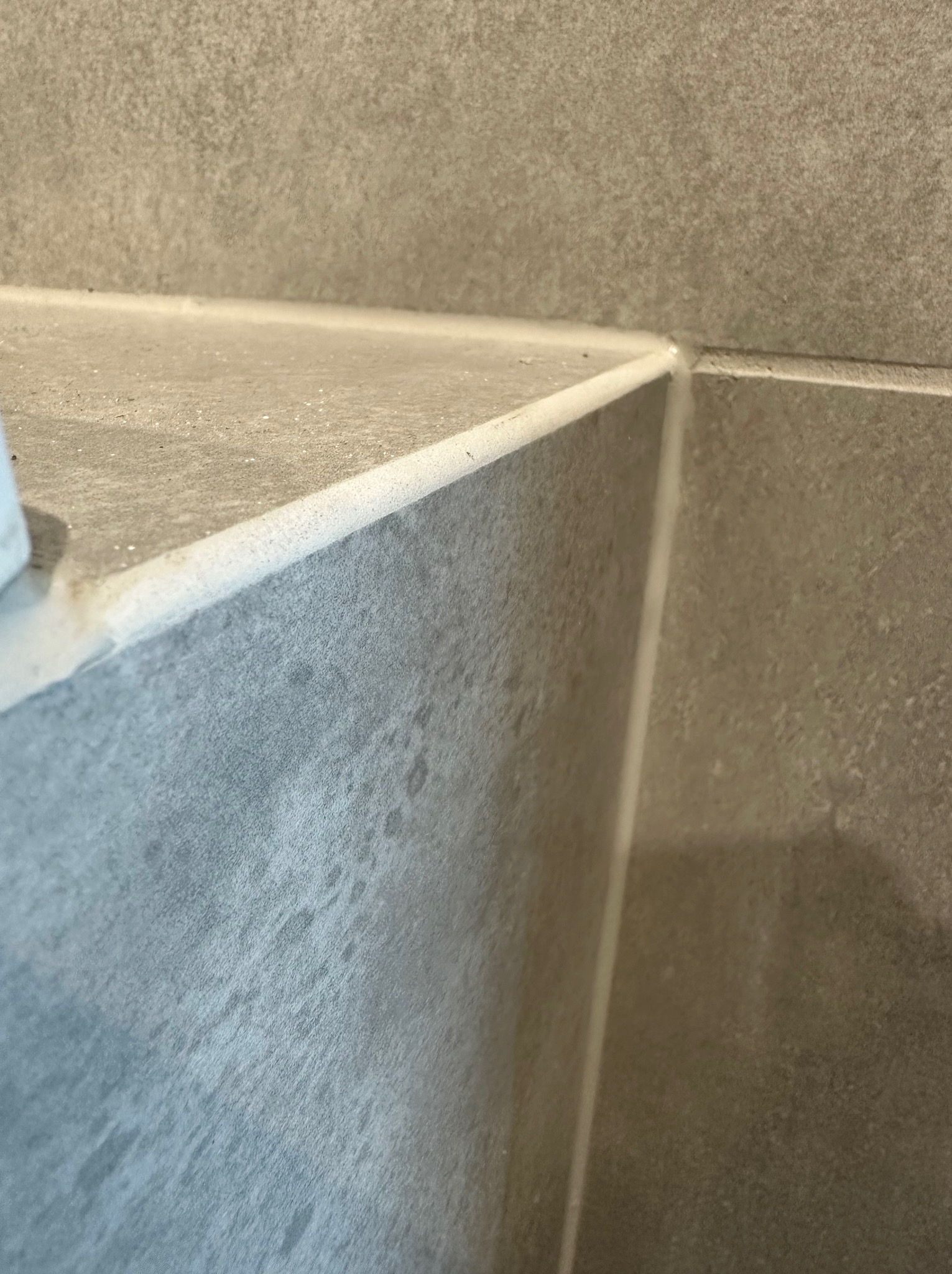 Szczegółowe ujęcie narożnika obłożonego szarymi płytkami ceramicznymi z widoczną fugą silikonową, ukazujące fakturę i precyzję wykonania.