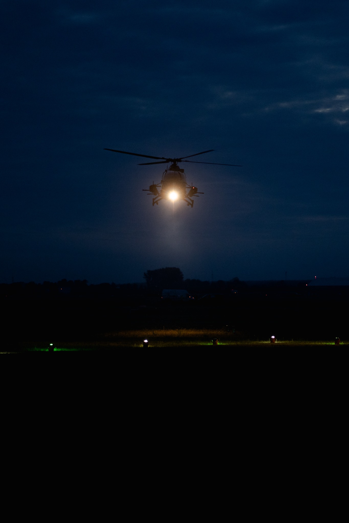 Nocny start helikoptera z lotniska w Poznaniu, oświetlonego lampami nawigacyjnymi, na tle ciemnego nieba z delikatnymi chmurami.
