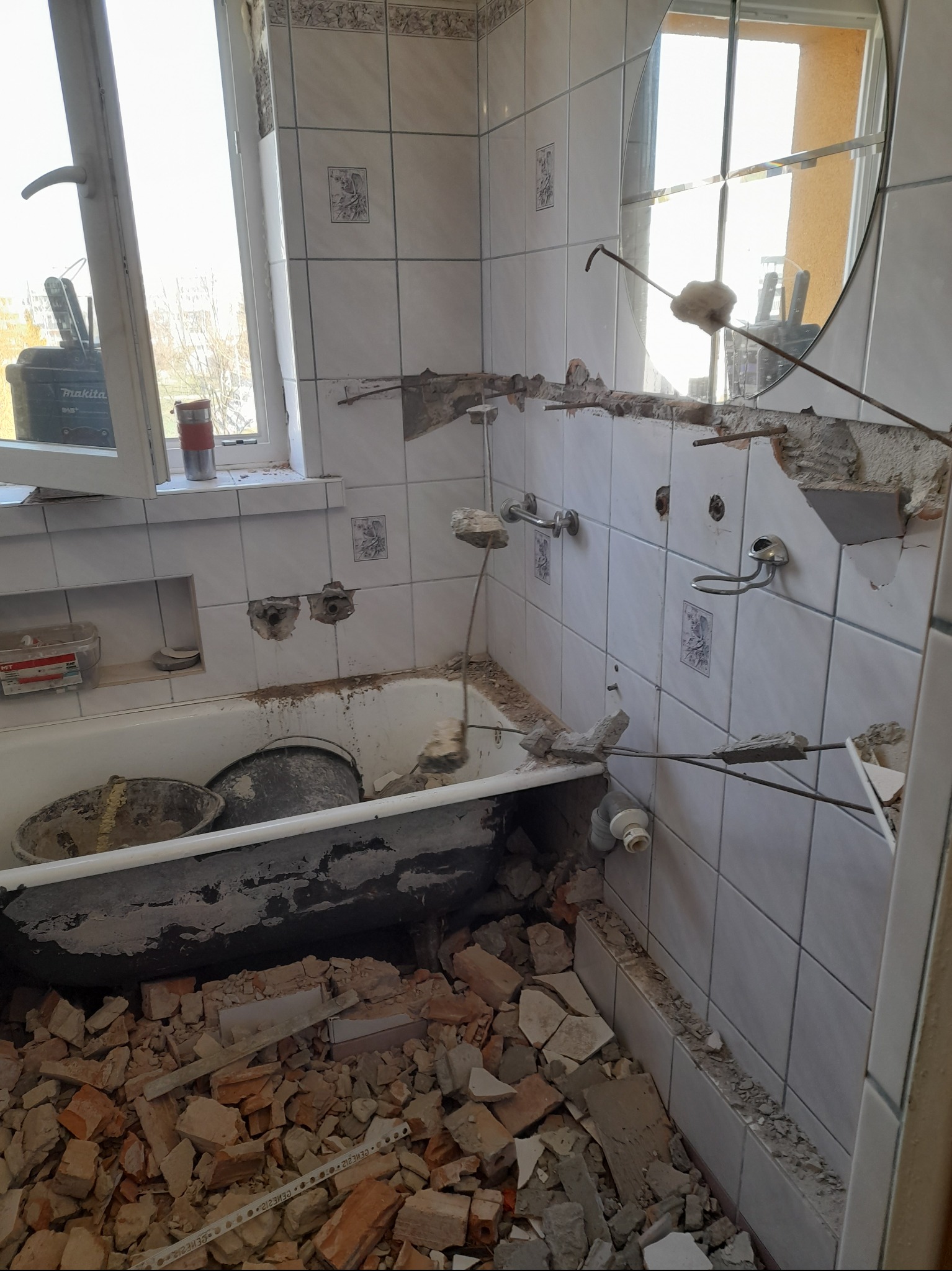 Demontaż płytek w łazience. Widoczna wanna, gruz, narzędzia i uszkodzone ściany. Etap przygotowawczy do prac wykończeniowych. Ujęcie z bliska, naturalne światło.