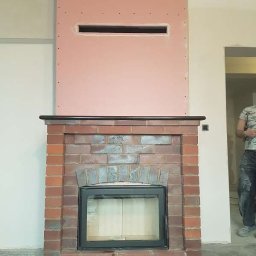 Kominki Mikam - Murowany kominek z czarnym wkładem i obudową z płyty kartonowo-gipsowej w trakcie montażu, widoczne niedoskonałości wykończenia i otwór wentylacyjny.