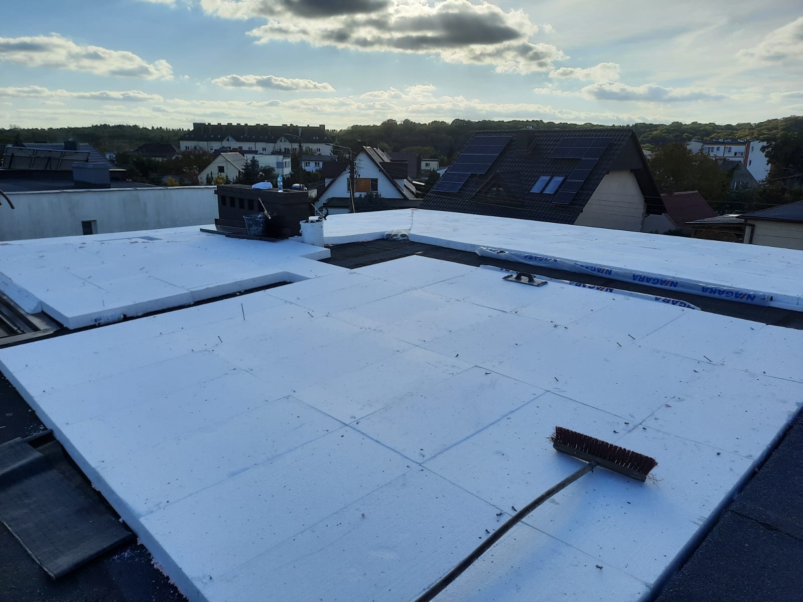 Ocieplenie dachu styropianem w trakcie realizacji w Koronowie, widoczny komin, narzędzia i fragmenty papy na dachu.