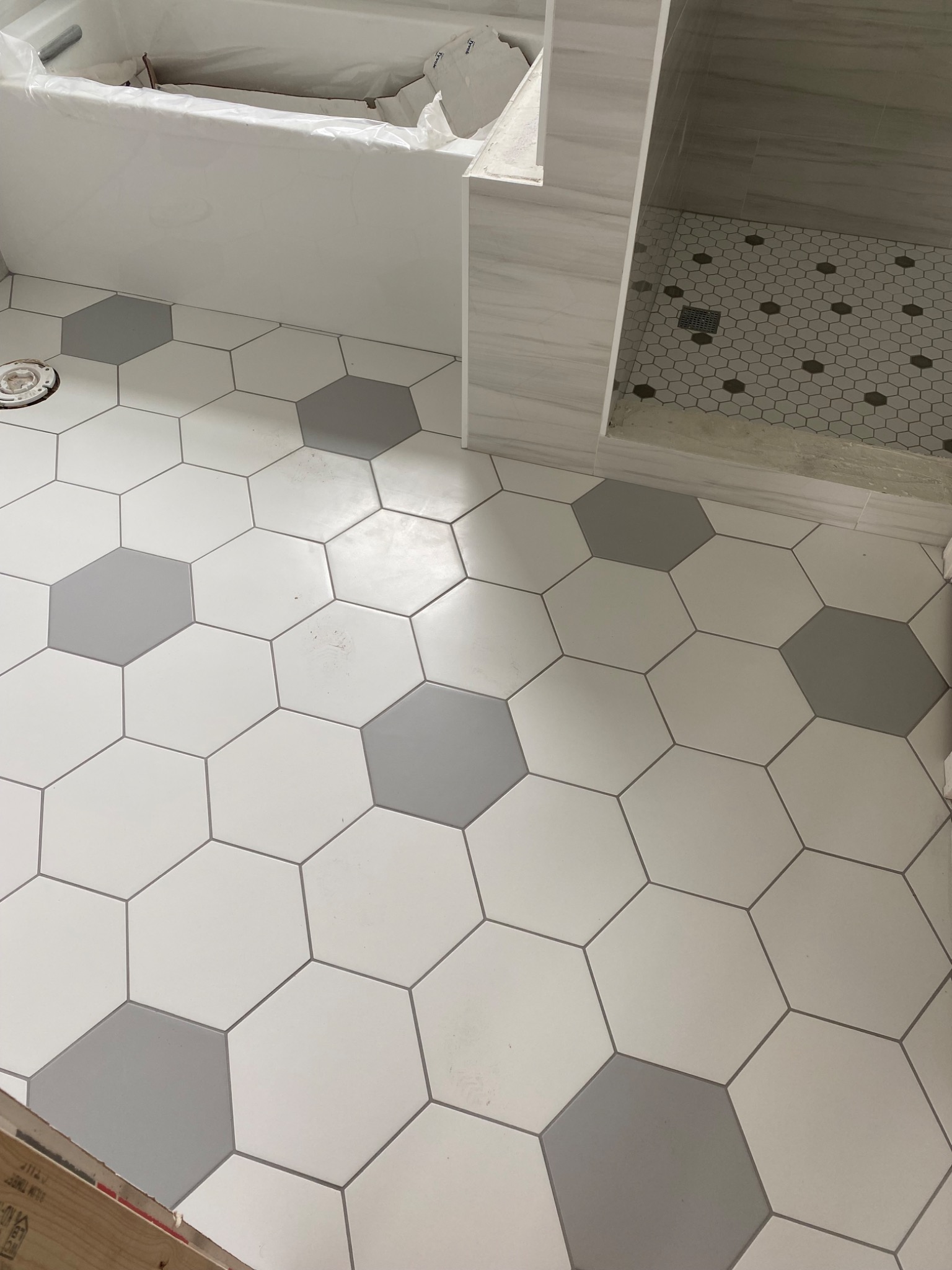 Ukończona podłoga w łazience z heksagonalnymi płytkami w odcieniach szarości i bieli, widoczny brodzik z mozaiką. Minimalistyczny design.