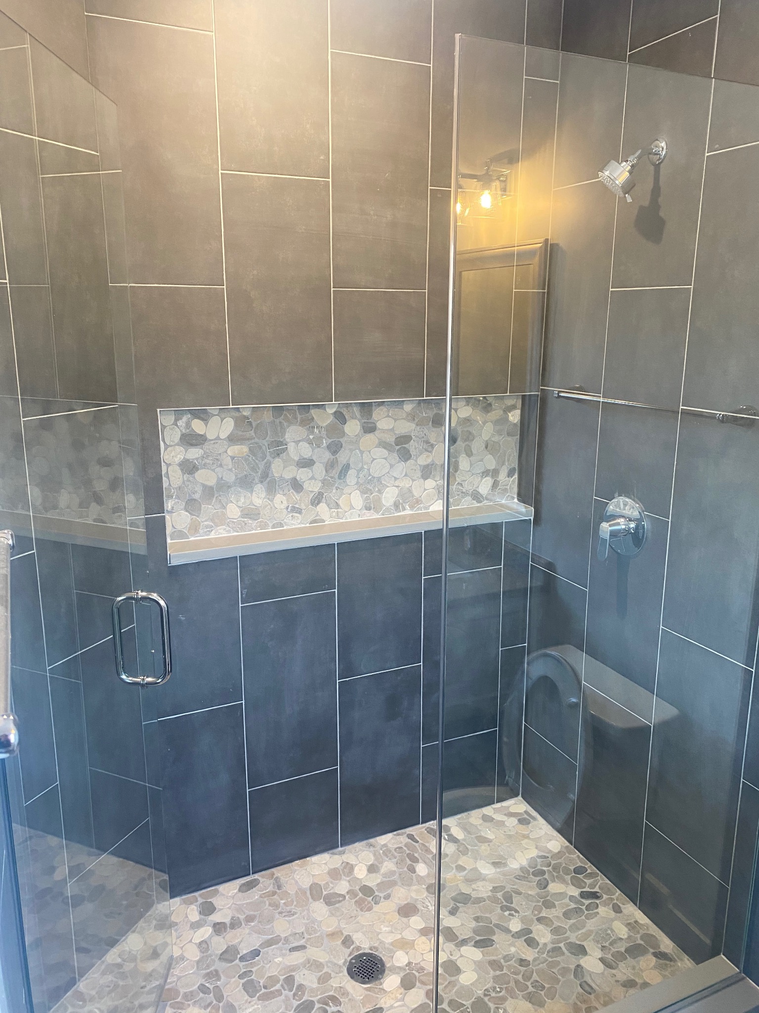 Nowoczesna kabina prysznicowa z szarymi płytkami i mozaiką z kamieni. Szklane drzwi, chromowana armatura. Wykończenie wnętrza łazienki w minimalistycznym stylu.