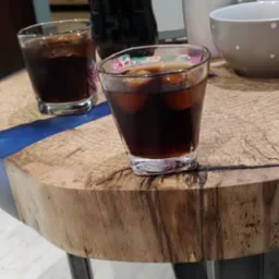 Okrągły stolik kawowy z blatem z surowego drewna z żywicą epoksydową w kolorze niebieskim, na kt&oacute;rym stoją dwie szklanki z napojem i lodu oraz miska w kropki