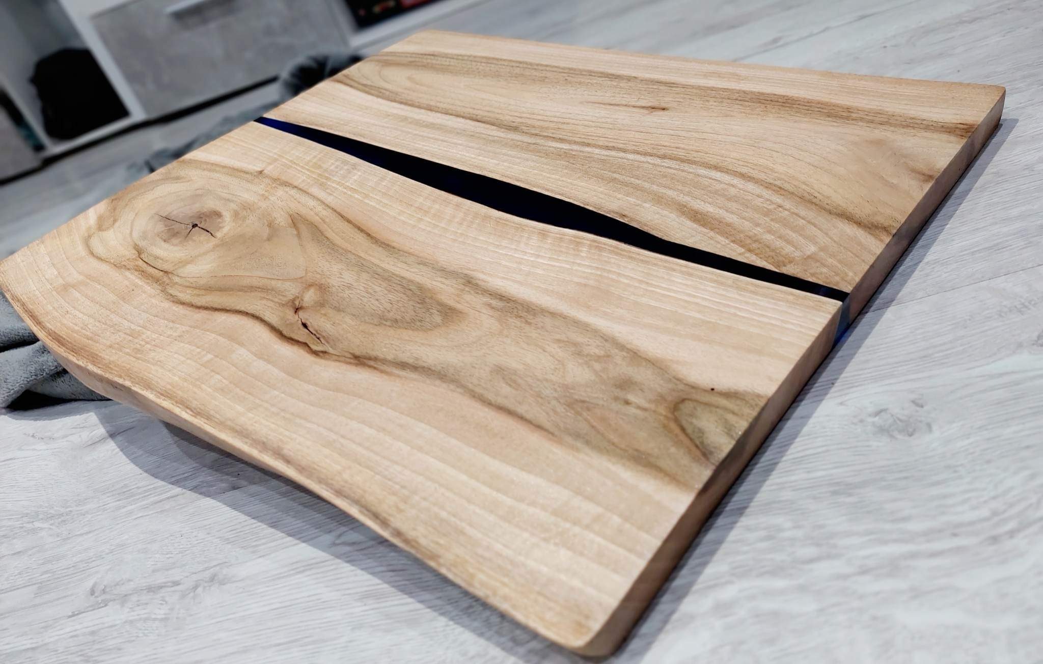 Deska z jasnego drewna z żywicą epoksydową w kolorze głębokiej czerni, widoczny rysunek słojów i naturalne sęki.