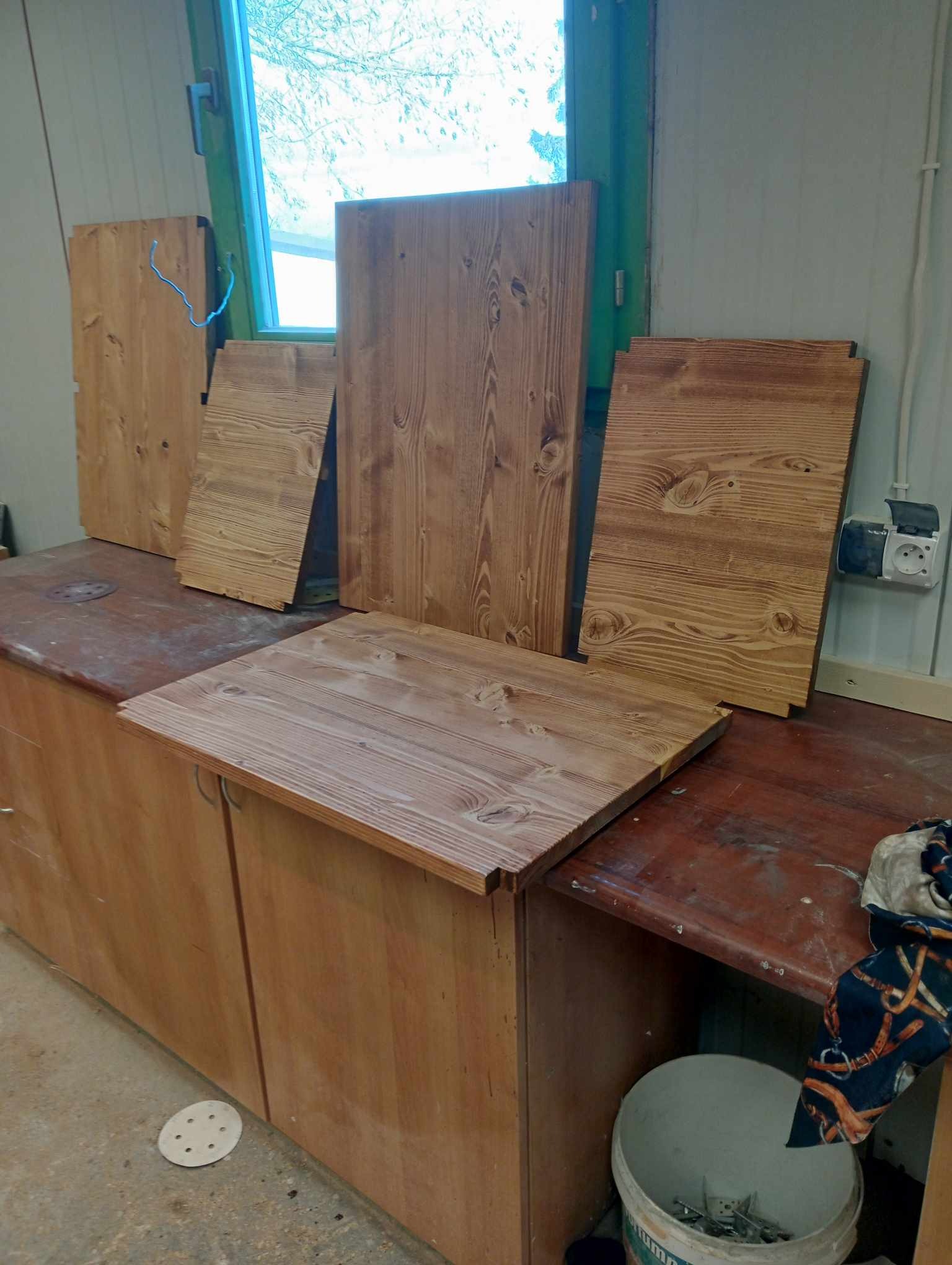 Przygotowane drewniane elementy, prawdopodobnie fronty meblowe, leżące na blacie w warsztacie, widoczne ślady obróbki i niedoskonałości.