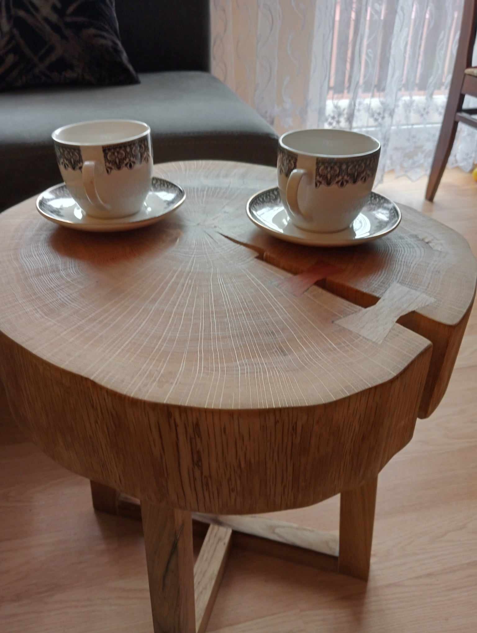 Stolik kawowy wykonany z pnia drzewa z widocznymi słojami, połączony na wpust jaskółczy ogon, z dwiema filiżankami na wierzchu, ustawiony na drewnianej podłodze.