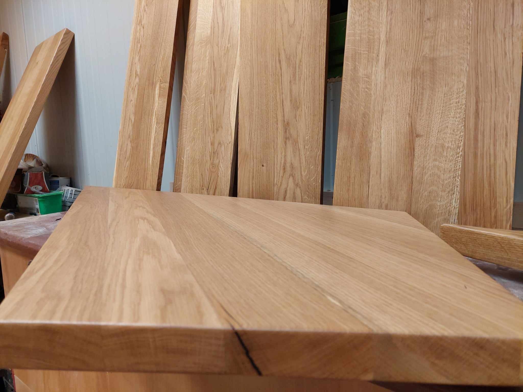 Przygotowane do montażu blaty i panele z jasnego drewna dębowego, widoczne naturalne usłojenie i sęki, obróbka stolarska w warsztacie.