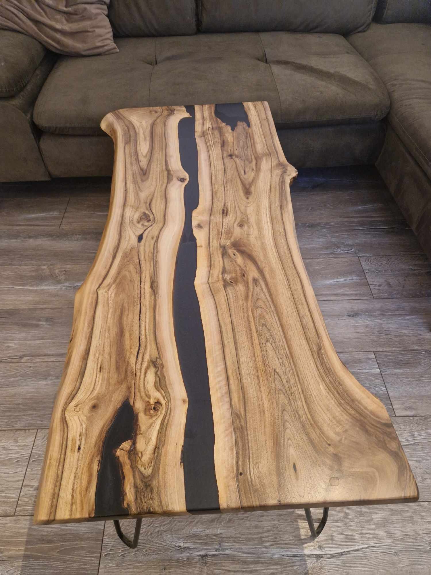 Stolik kawowy z blatem z naturalnego drewna z żywicą epoksydową w kolorze czarnym, na metalowych nóżkach, ustawiony na podłodze z paneli.