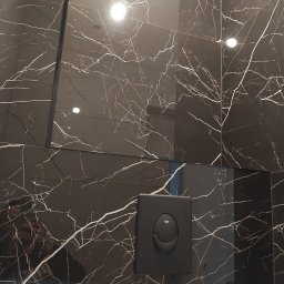 KONDIX KONRAD KOZUBSKI - Czarne płytki marmurowe z białymi żyłami w łazience, z widocznym przyciskiem spłuczki Grohe. Nowoczesny design, wykończenie z połyskiem.