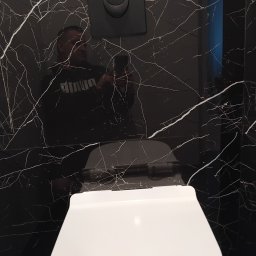 KONDIX KONRAD KOZUBSKI - Nowoczesna toaleta podwieszana z czarną płytką imitującą marmur z białymi żyłami, widoczny czarny przycisk spłuczki Grohe i odbicie osoby robiącej zdjęcie.