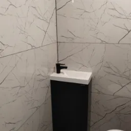 Nowoczesna łazienka z umywalką na szafce w kolorze czarnym, białą armaturą i płytkami imitującymi marmur na ścianach i podłodze. Minimalistyczny design.