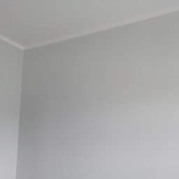 Kamil Stolat - Świeżo pomalowany narożnik pokoju na szaro z białą listwą przysufitową.