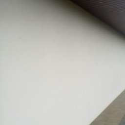 Kamil Stolat - Świeżo pomalowana, jasna elewacja budynku z widocznym fragmentem drewnianego podbitki dachowej i chodnika z kostki brukowej u dołu zdjęcia.