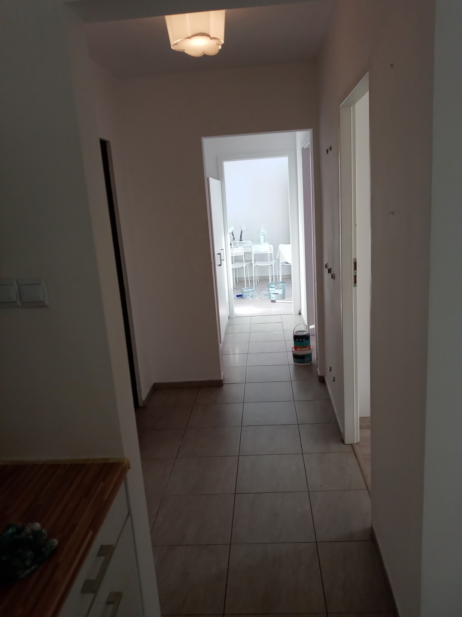 Korytarz w trakcie malowania: widoczne wiaderka z farbą na podłodze, białe ściany i drzwi, w głębi pokój z meblami zabezpieczonymi folią malarską.