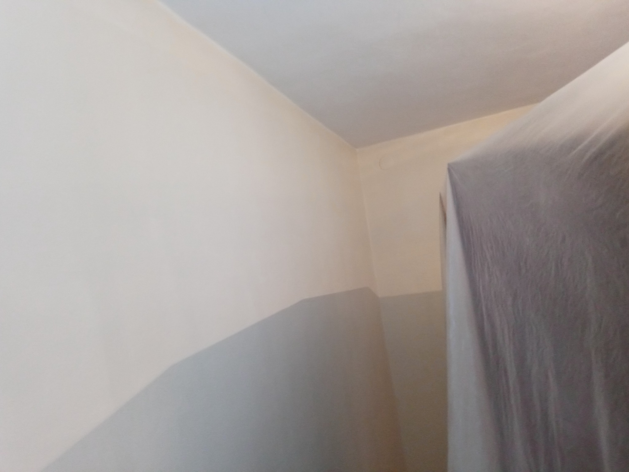 Świeżo pomalowane wnętrze z dwukolorową ścianą, górna część kremowa, dolna szara, zabezpieczone folią meble w rogu pomieszczenia.