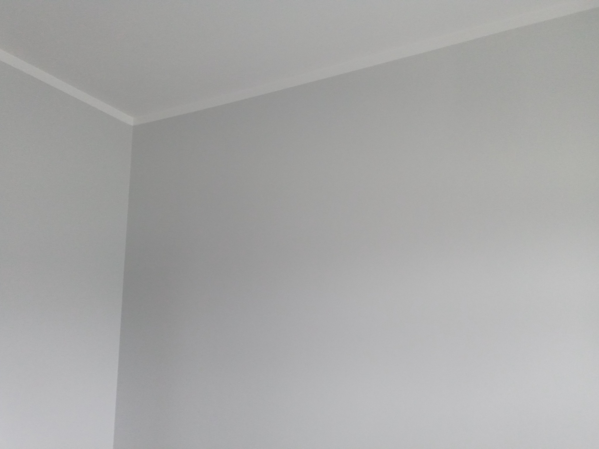 Świeżo pomalowany narożnik pokoju na szaro z białą listwą przysufitową.