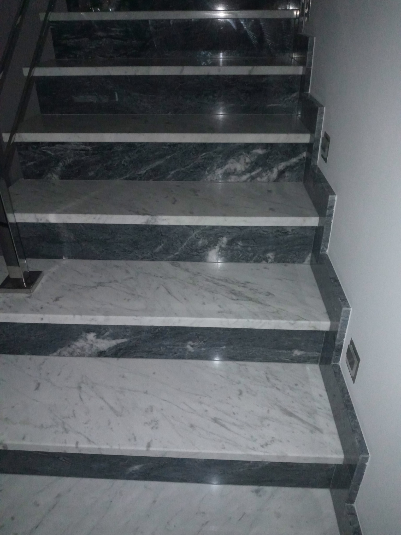 Schody wykończone białym i szarym marmurem z metalową balustradą, widok z góry na stopnie.