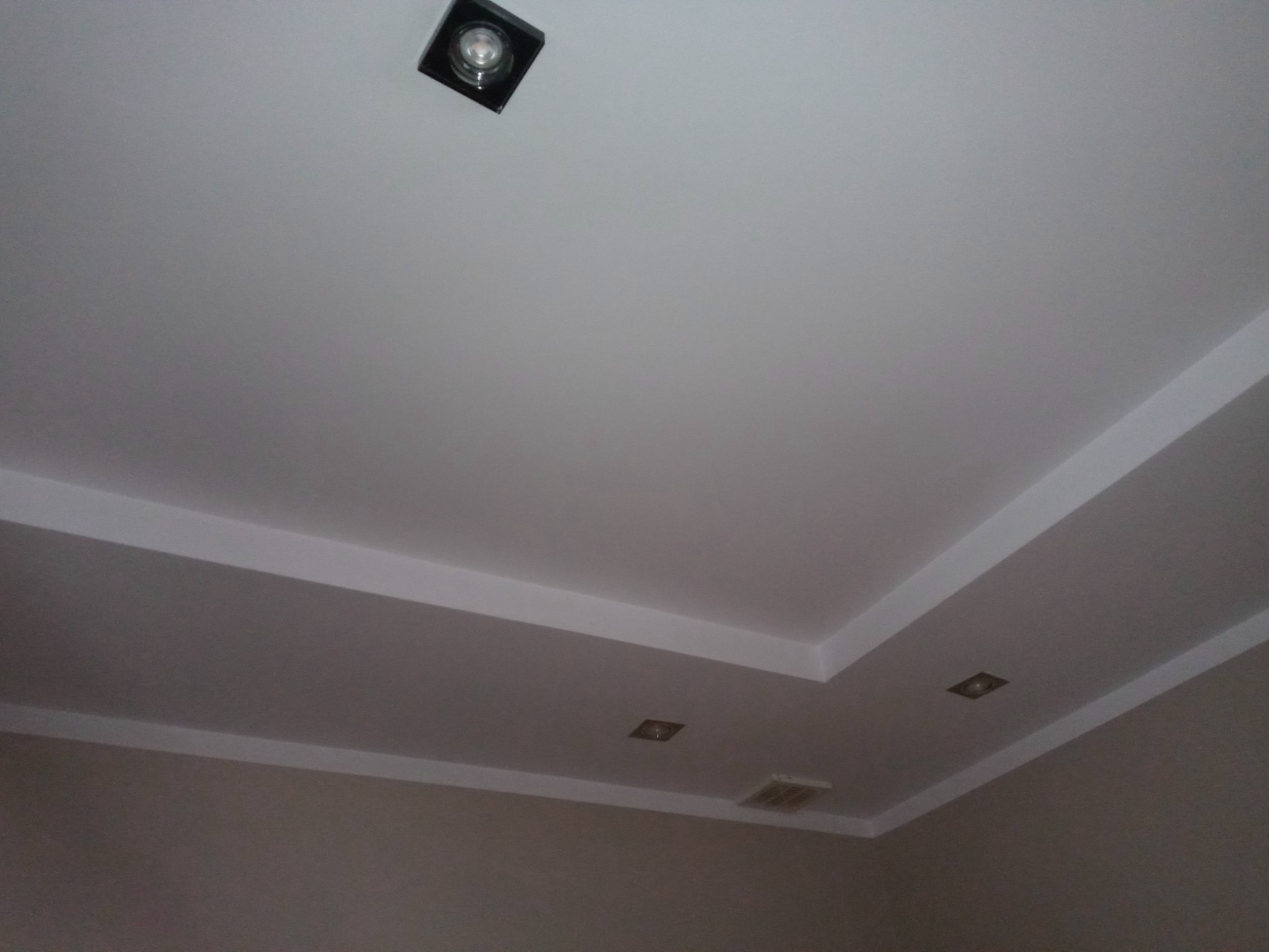 Biały sufit po remoncie z zamontowanymi, kwadratowymi lampami halogenowymi i kratką wentylacyjną przy ścianie.