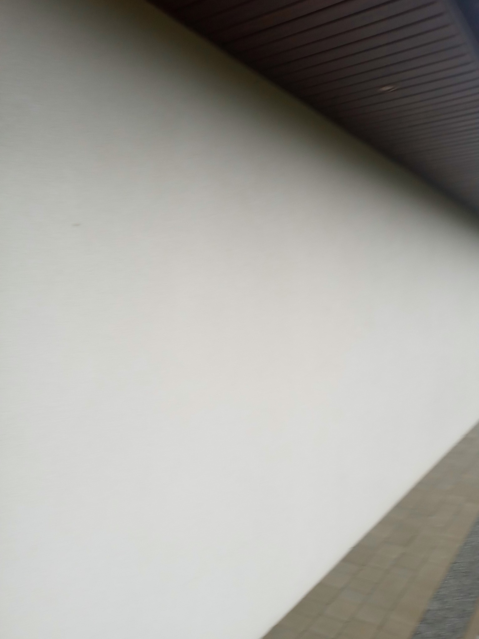 Świeżo pomalowana, jasna elewacja budynku z widocznym fragmentem drewnianego podbitki dachowej i chodnika z kostki brukowej u dołu zdjęcia.