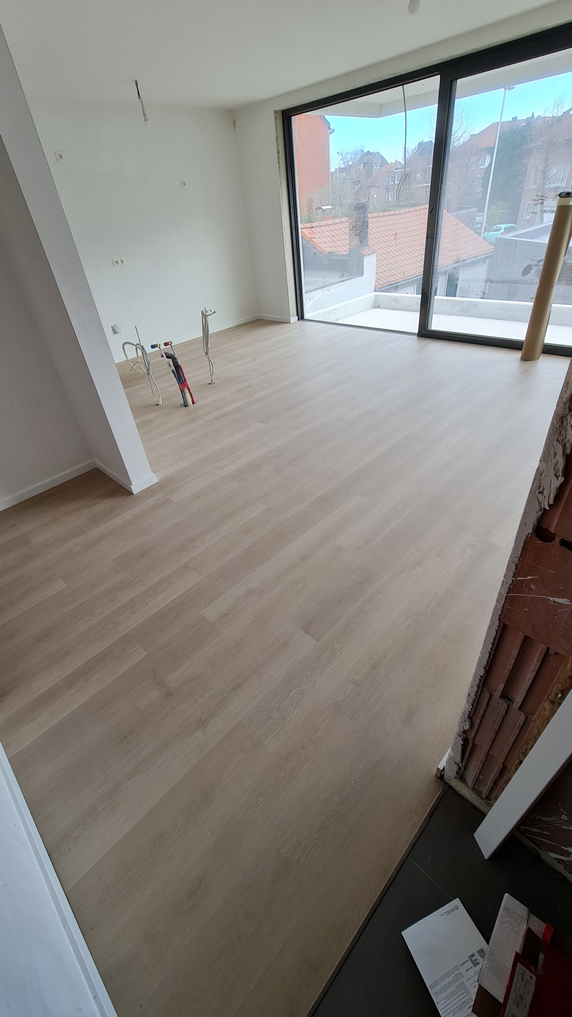 Jasne panele podłogowe ułożone w nowym mieszkaniu w Nieszawie, widoczne narzędzia i niedokończone wykończenie ściany.