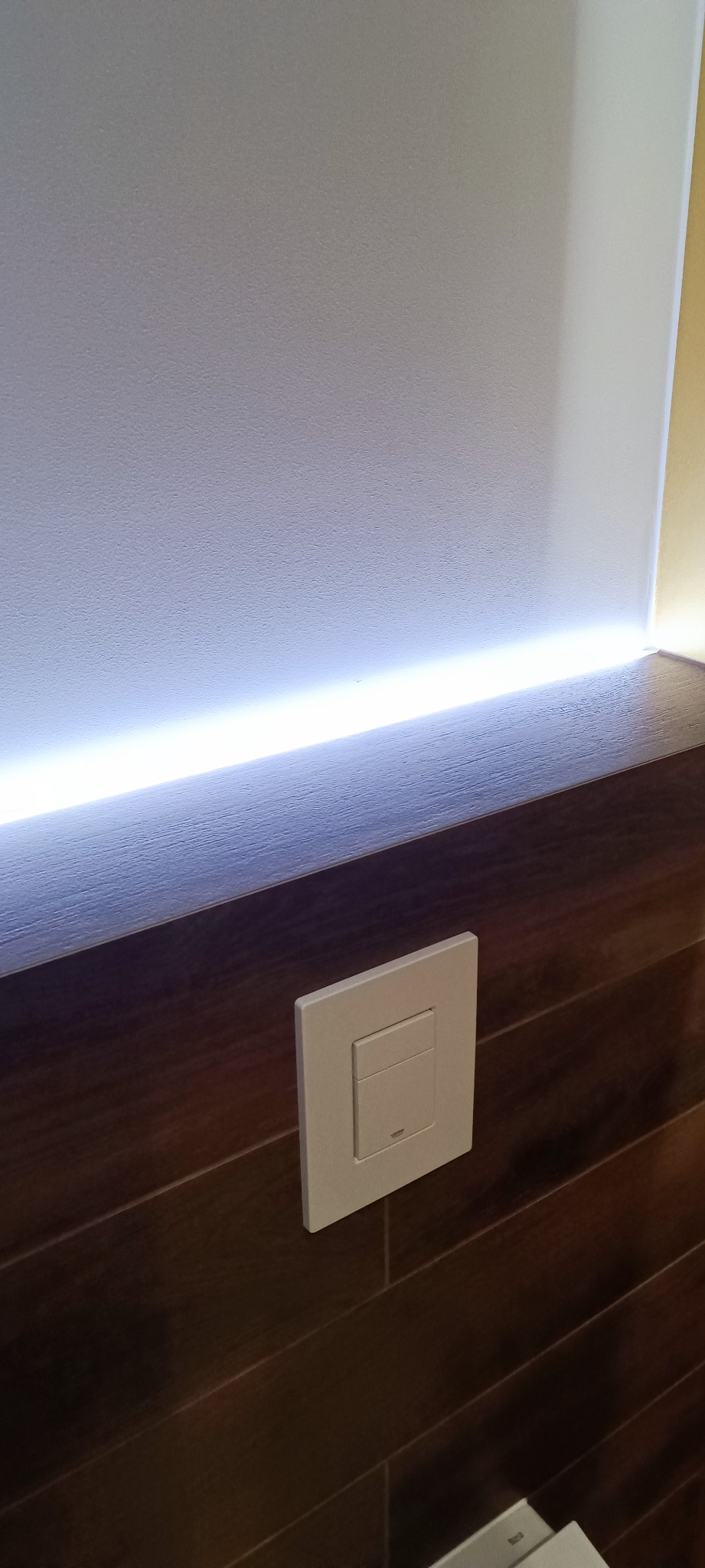 Ściana wykończona drewnopodobnymi płytkami z podświetleniem LED i włącznikiem światła Grohe.