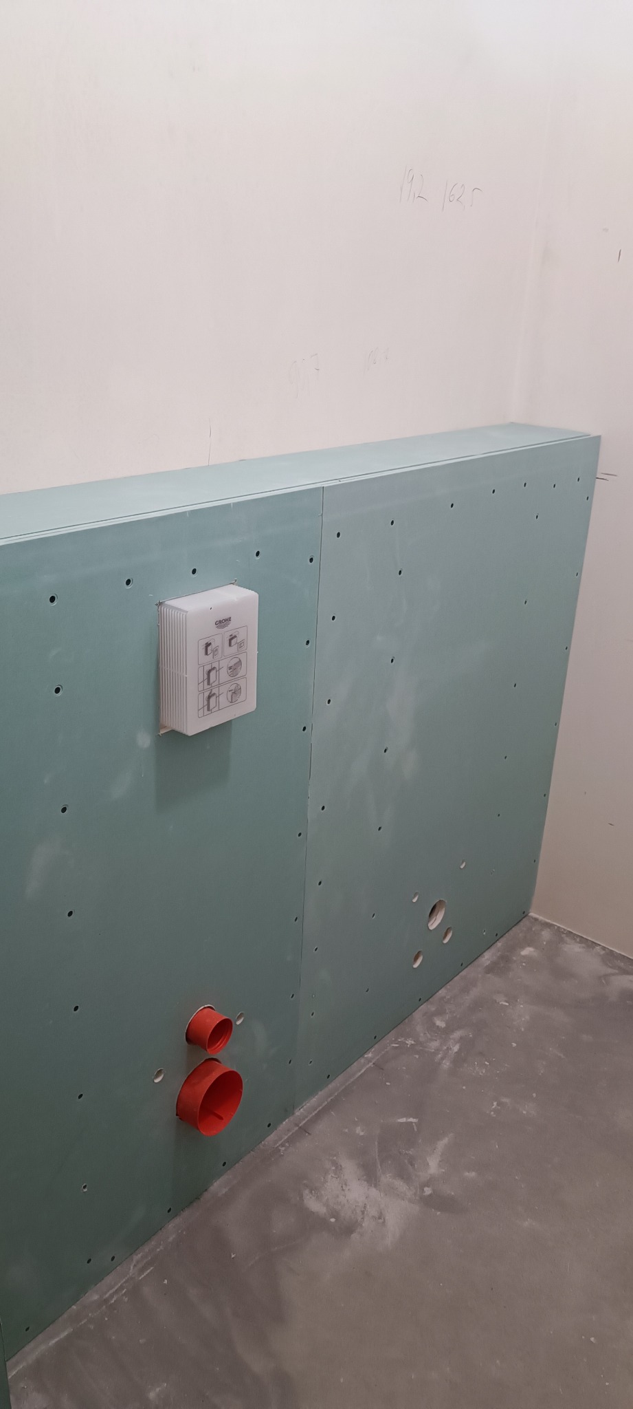 Stelaż z płyty karton-gips w łazience, widoczne otwory na instalacje, zamontowana puszka Grohe ze schematem montażu, surowy beton na podłodze.