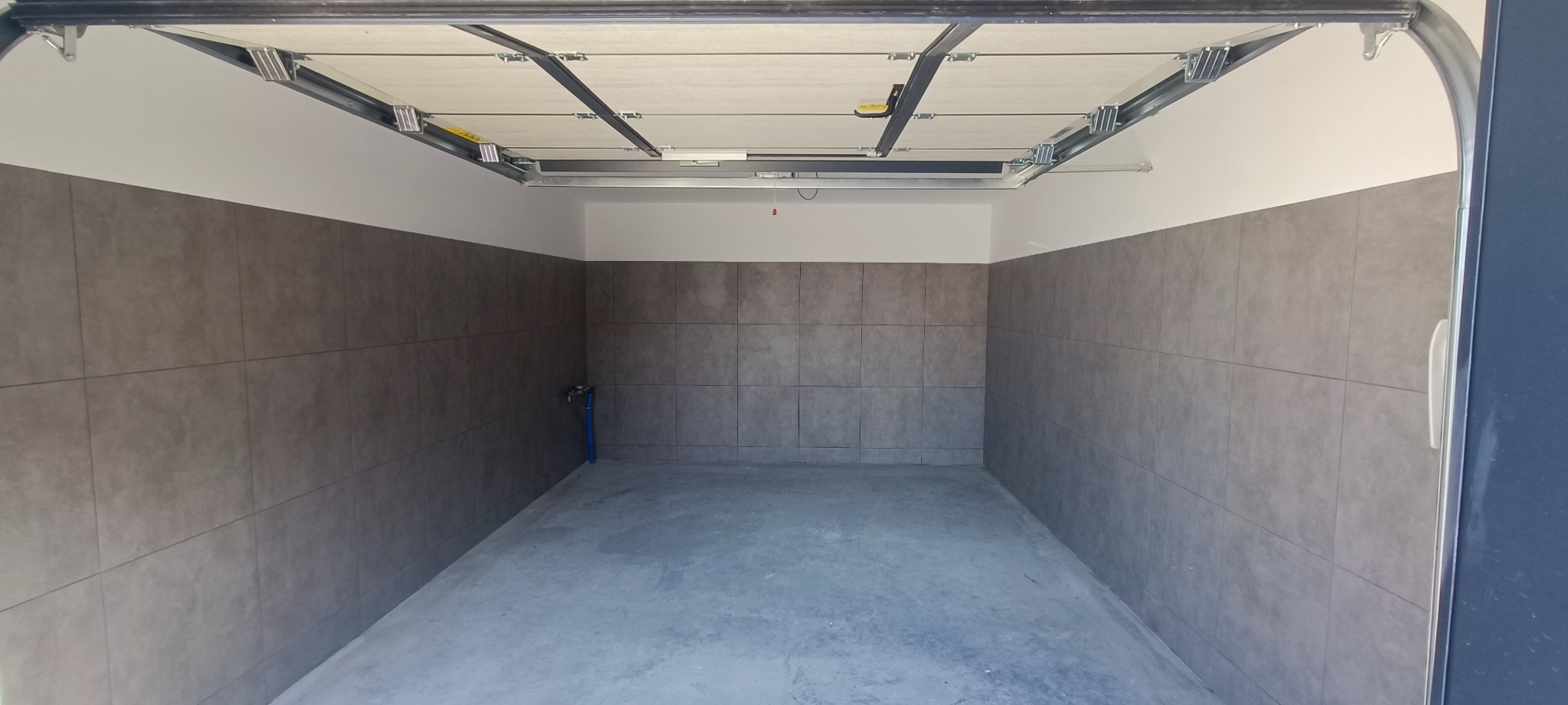 Wykafelkowane ściany garażu z instalacją wodną, widok z zewnątrz z otwartą bramą garażową.