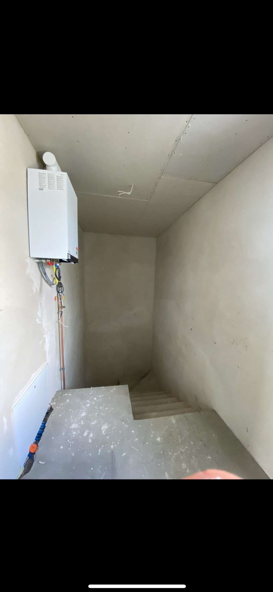 Surowe wnętrze klatki schodowej w trakcie remontu, widoczne płyty karton gips na ścianach i suficie, instalacja grzewcza i schody pokryte resztkami gładzi.