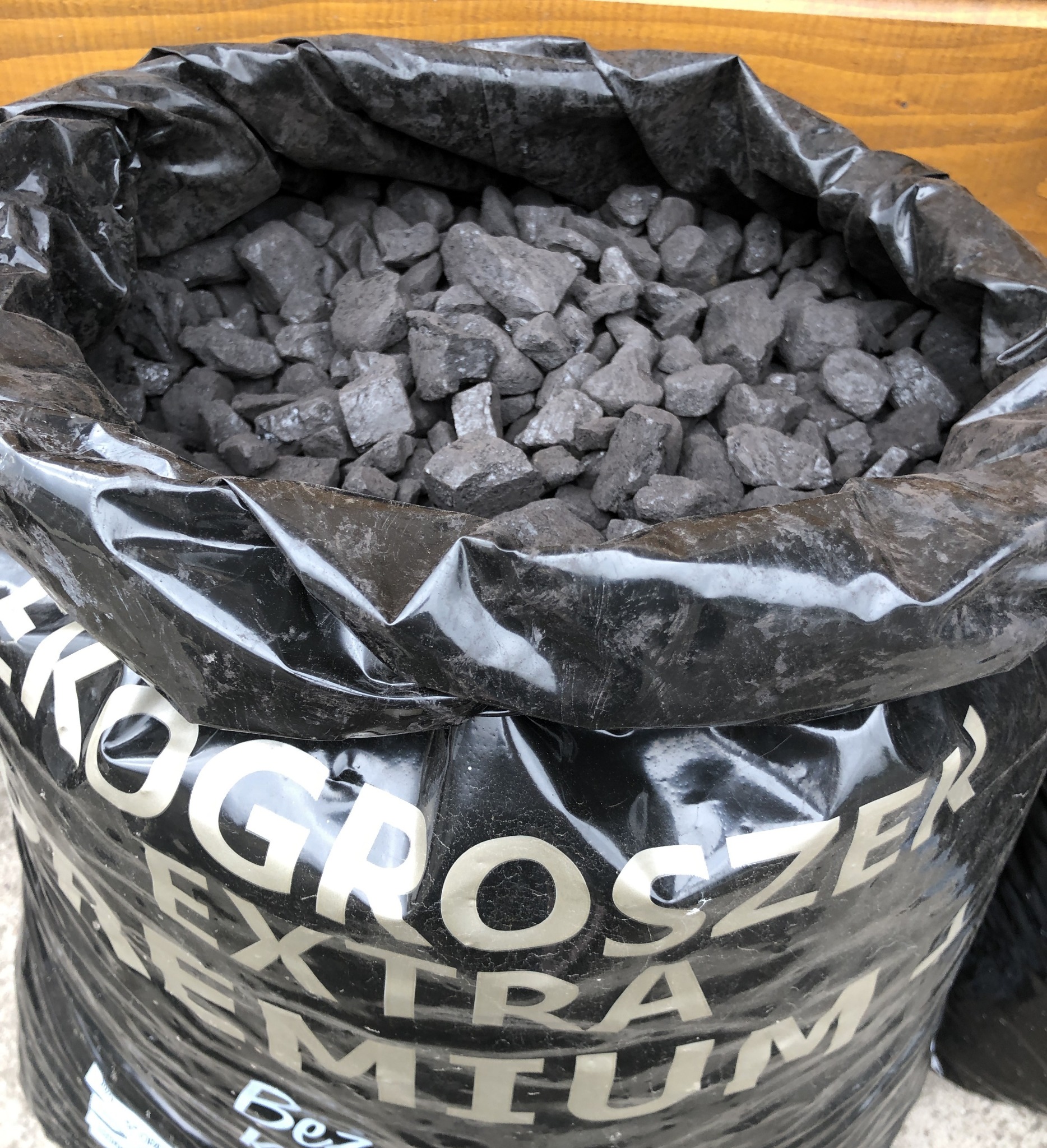 Worek z czarnego, błyszczącego tworzywa wypełniony bryłkami węgla, z widocznym napisem 'EKOGROSZEK EXTRA PREMIUM' w kolorze białym.