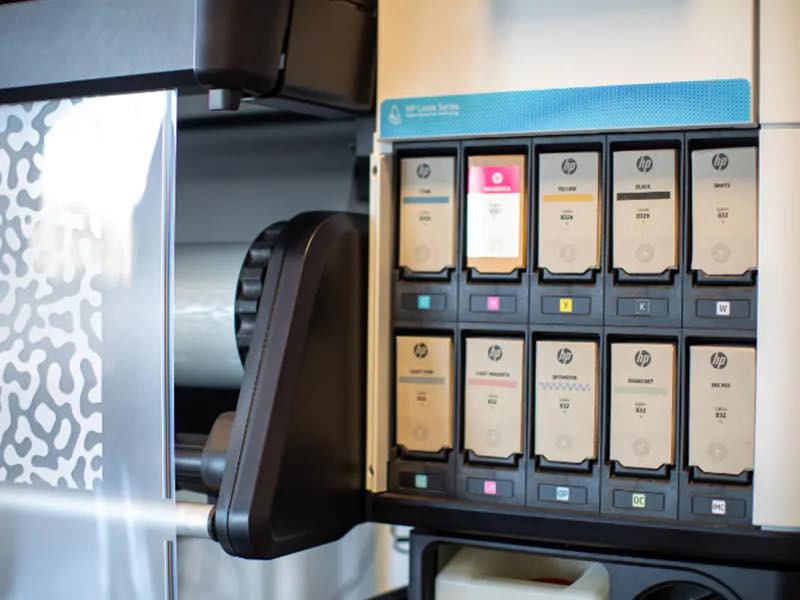 Wnętrze drukarki wielkoformatowej HP Latex Series z otwartą komorą na kartridże z tuszem: Cyan, Magenta, Yellow, Black, White, Light Cyan, Light Magenta, Optimizer, Overcoat, Ink Maintenance Cartridge