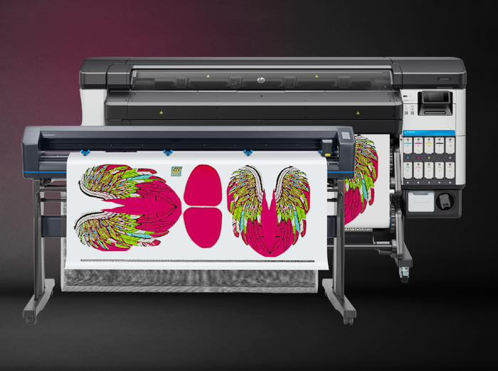 Dwa plotery drukujące na białym materiale grafiki skrzydeł i owali w kolorach różu, zieleni i żółci na ciemnym tle.