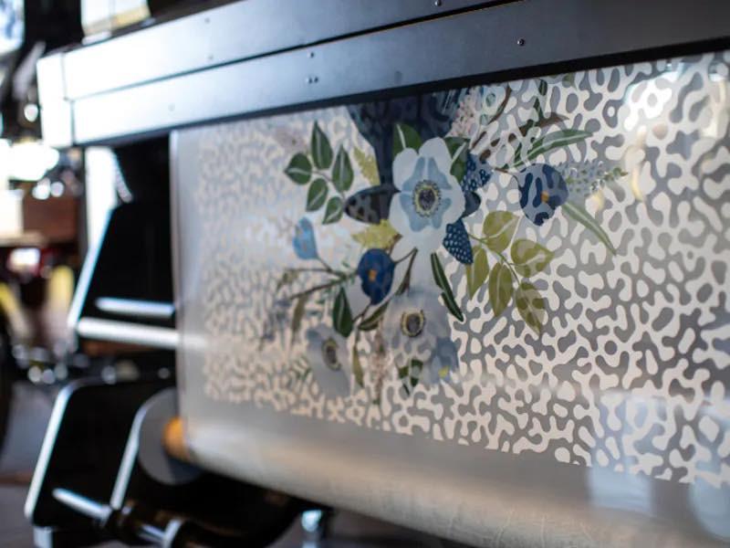 Drukarka wielkoformatowa w trakcie nanoszenia wzoru kwiatowego na materiał z abstrakcyjnym tłem.